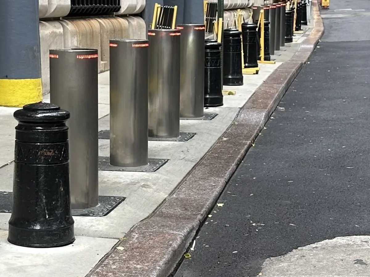 Several metal bollards along a sidewalk, acting as barriers to prevent vehicle access.