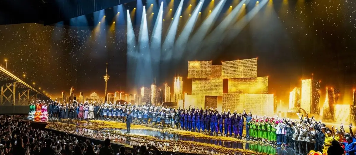 Performers stand on a brightly lit stage at MGM Cotai Theater, illuminated by dynamic lighting effects.