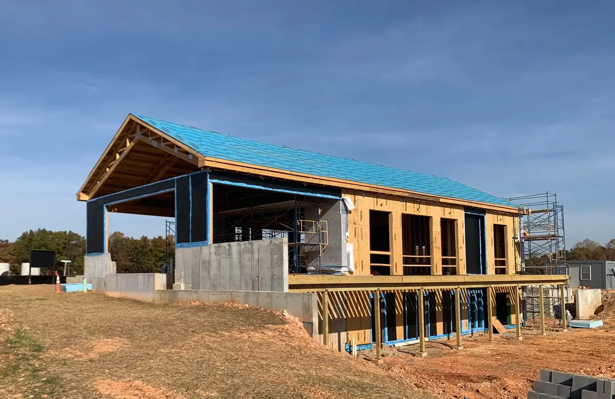 Progress photo of the Watershed Community Center clubhouse under construction, featuring a wooden framework and partially completed exterior walls