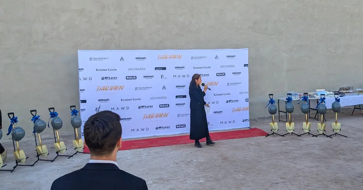 A speaker addressing the crowd during the 45-40 Vernon Boulevard groundbreaking ceremony in front of a sponsor banner.